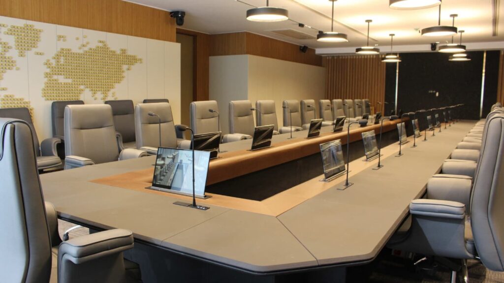 Sala de juntas corporativa equipada con pantallas elevables HD ultrafinas VISSONIC integradas en la mesa, micrófonos empotrados y diseño premium