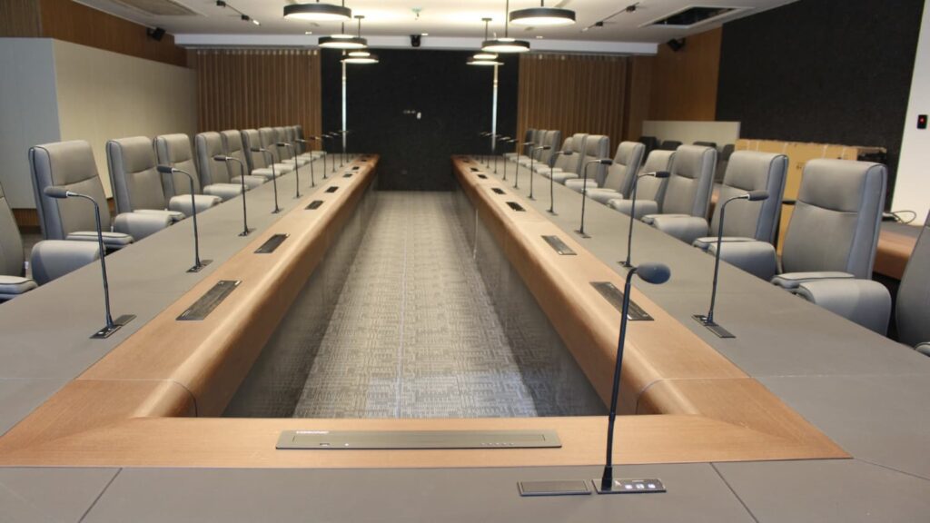 Vista panorámica de sala de reuniones ejecutiva con pantallas elevables ultrafinas VISSONIC ocultas en la mesa y sistema de debate empotrado