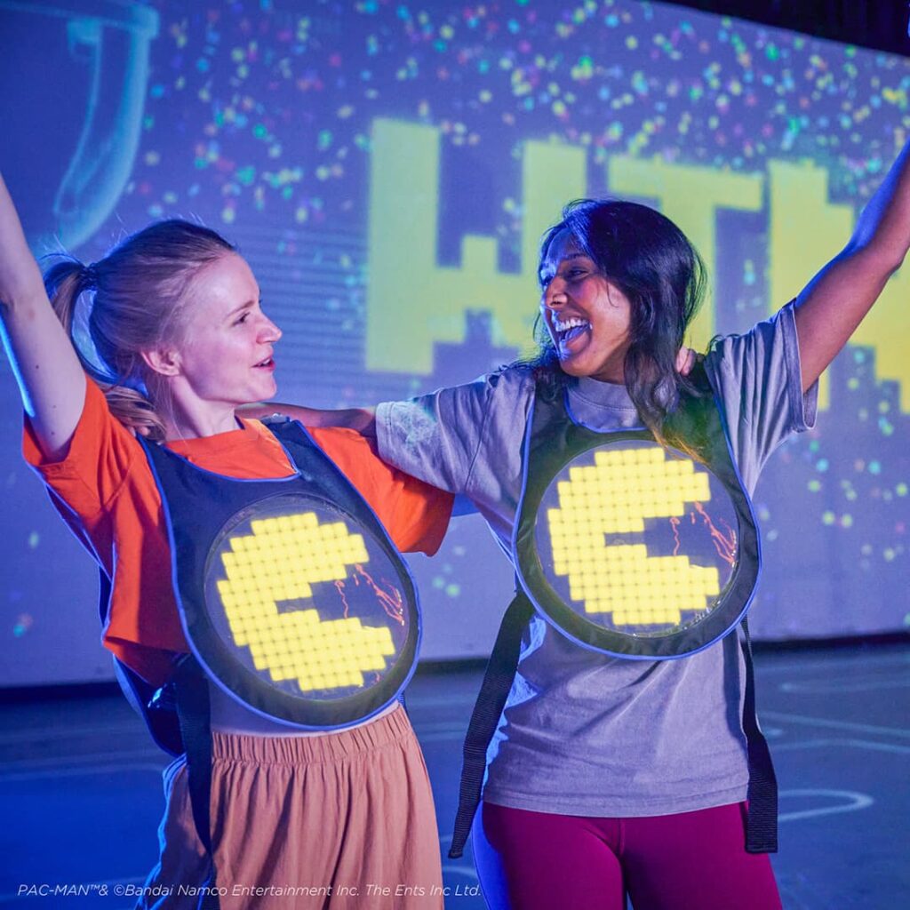 Jugadoras celebrando en PAC-MAN LIVE EXPERIENCE, equipadas con sensores del sistema de tracking BlackTrax de CAST.