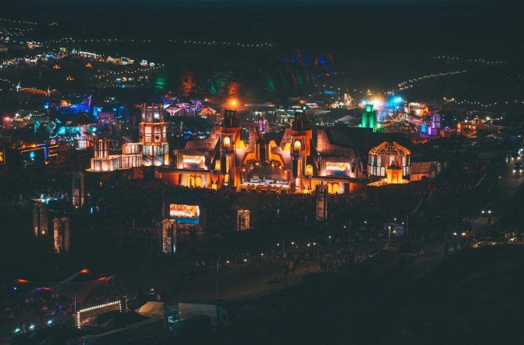 Vista aérea nocturna del Boomtown Festival 2025 con escenarios iluminados y diseño escénico multicolor.
