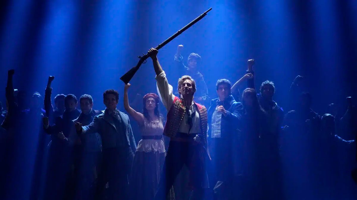 Meyer Sound en Los Miserables en una escena del musical en el Teatro Nuevo Apolo, con el protagonista alzando un fusil entre el elenco bajo luz azul.