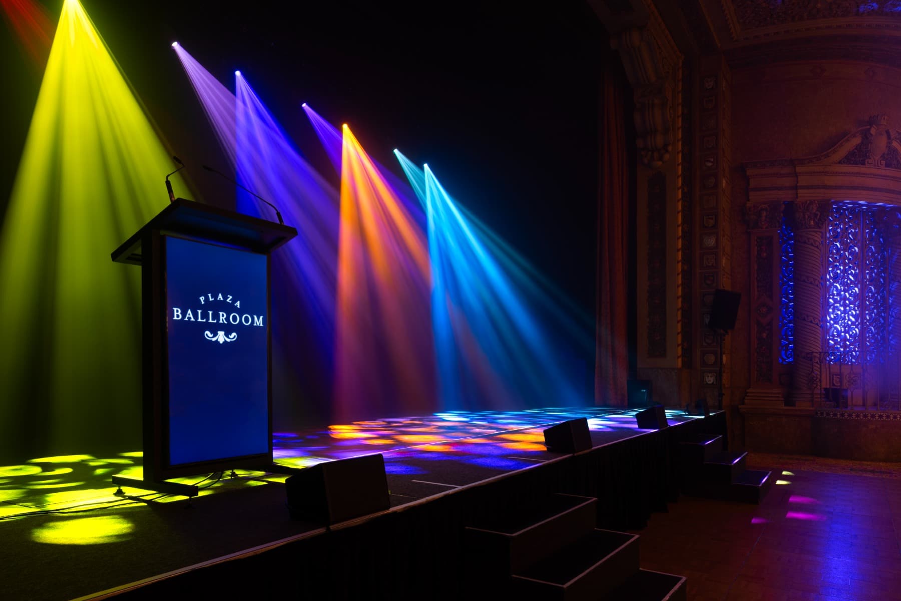 Podio iluminado en el Marriner Theatre Plaza Ballroom, transformado por Clearlight Shows con efectos de iluminación Infinity y Showtec, ideal para presentaciones y eventos en vivo.