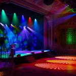 Pista de baile del Marriner Theatre Plaza Ballroom iluminada con efectos de luces Infinity y Showtec, creando un ambiente vibrante y colorido para eventos y espectáculos en vivo.