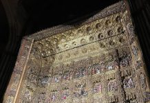 Retablo mayor de la Catedral de Sevilla iluminado durante el espectáculo “El Evangelio de la Madera”, con detalles dorados y escenas bíblicas esculpidas.