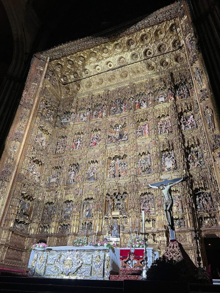 Retablo mayor de la Catedral de Sevilla iluminado durante el espectáculo “El Evangelio de la Madera”, con detalles dorados y escenas bíblicas esculpidas.