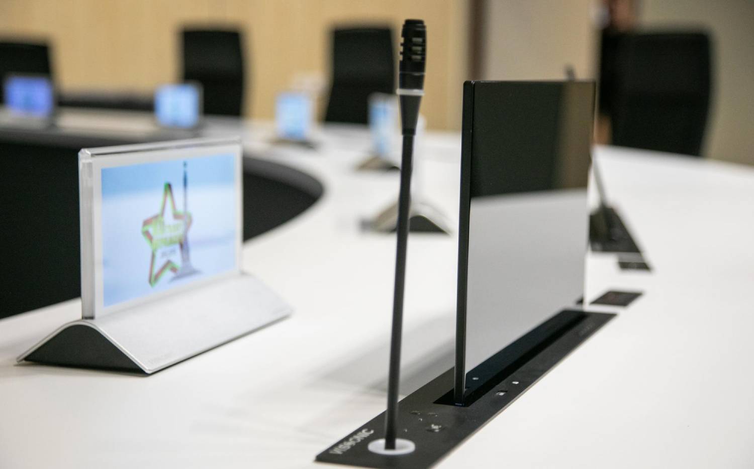 Detalle de la solución multilingüe para conferencias de VISSONIC con micrófono unidireccional y pantalla multimedia retráctil en sala VIP.