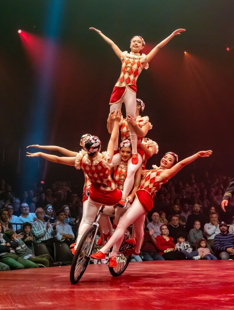 Artistas de Circlassica realizan una acrobacia grupal sobre un monociclo bajo la carpa iluminada con cabezas móviles Robe.