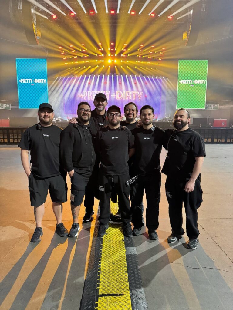 Equipo técnico de sonido de la gira mundial Maluma Pretty Dirty 2025 posando frente al escenario principal, con la producción de iluminación y pantallas LED activadas antes del show.