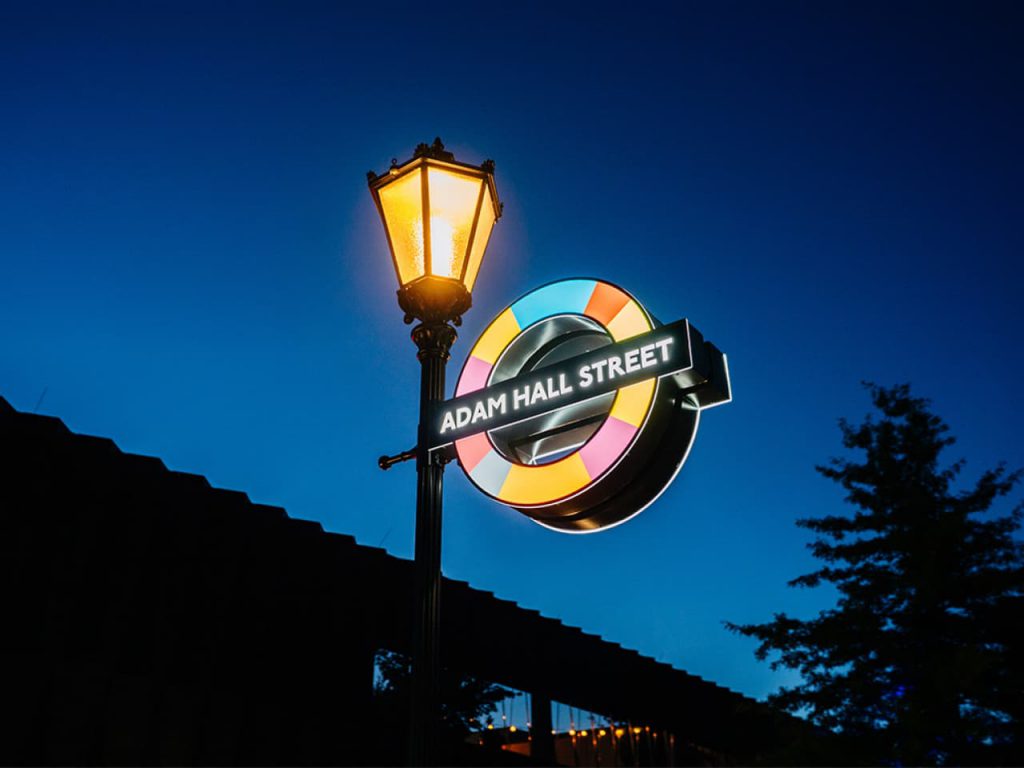 Señal luminosa de la parada “Adam Hall Street” frente al Experience Centre, creada para conmemorar el 50 aniversario de Adam Hall.