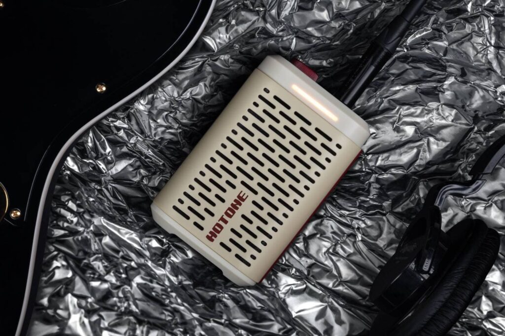 Amplificador de bolsillo Pulze Mini de Hotone junto a una guitarra eléctrica y auriculares, ideal para tocar y grabar en cualquier lugar.