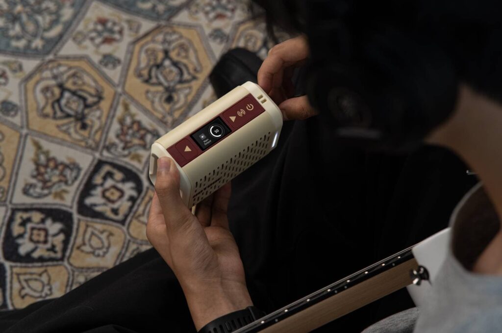 Músico ajustando parámetros en el Pulze Mini mientras ensaya con auriculares, demostrando su uso portátil y silencioso.