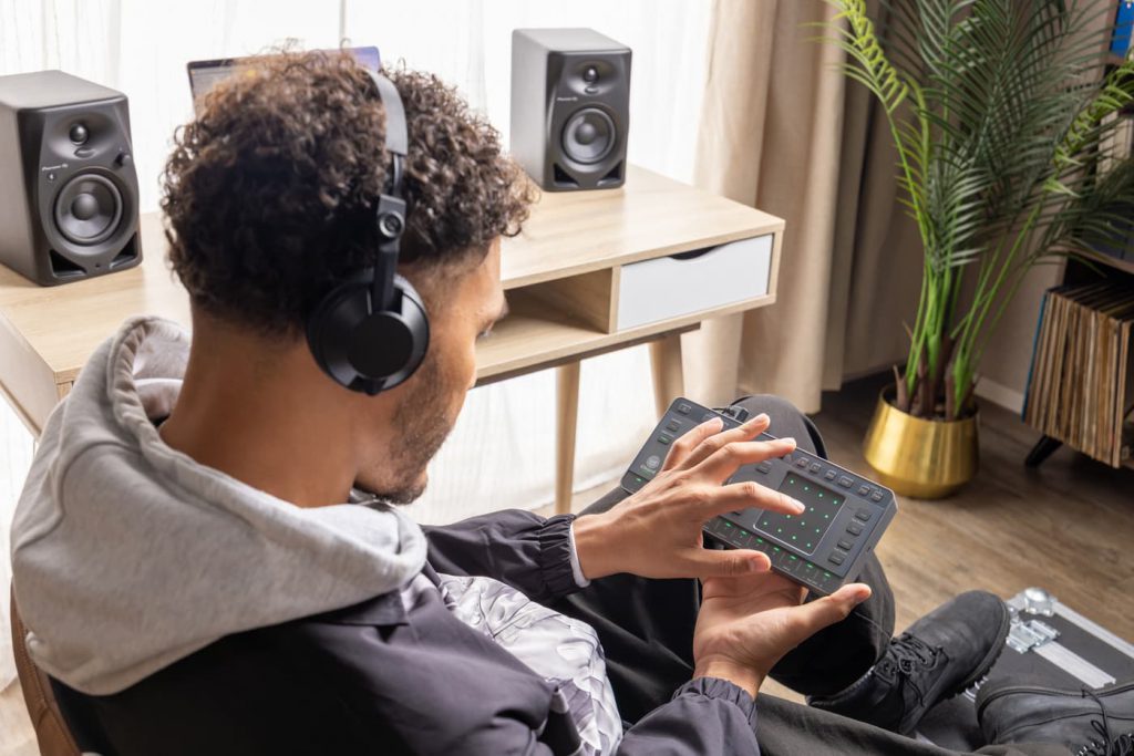 Músico usando la groovebox Chordcat en casa con auriculares, explorando acordes y creando música de forma intuitiva.
