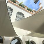 Velas tensadas equipadas con ABSORBRELLA instaladas en la terraza de un hotel urbano, mostrando su integración discreta en estructuras arquitectónicas exteriores.
