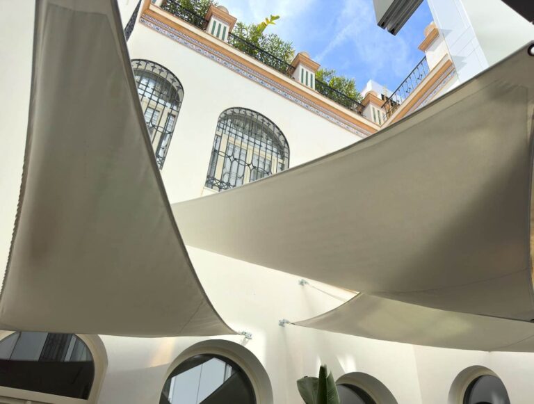 Velas tensadas equipadas con ABSORBRELLA instaladas en la terraza de un hotel urbano, mostrando su integración discreta en estructuras arquitectónicas exteriores.