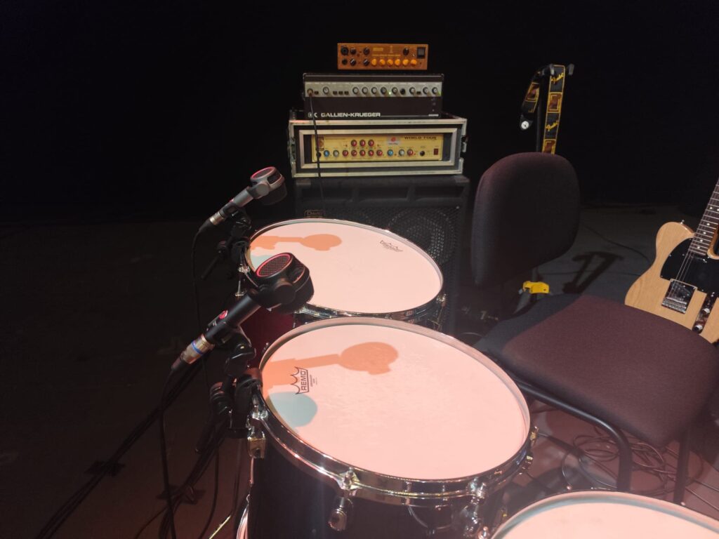 Micrófonos Austrian Audio instalados sobre batería y frente a amplificadores en el escenario del Teatro Victoria Eugenia para captación profesional de sonido.