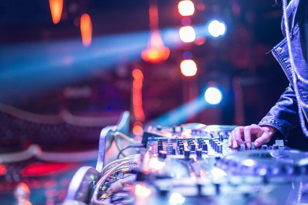DJ mezclando en cabina con efectos de luz creados por las mejores lámparas para iluminación de discotecas, clubs y DJ.