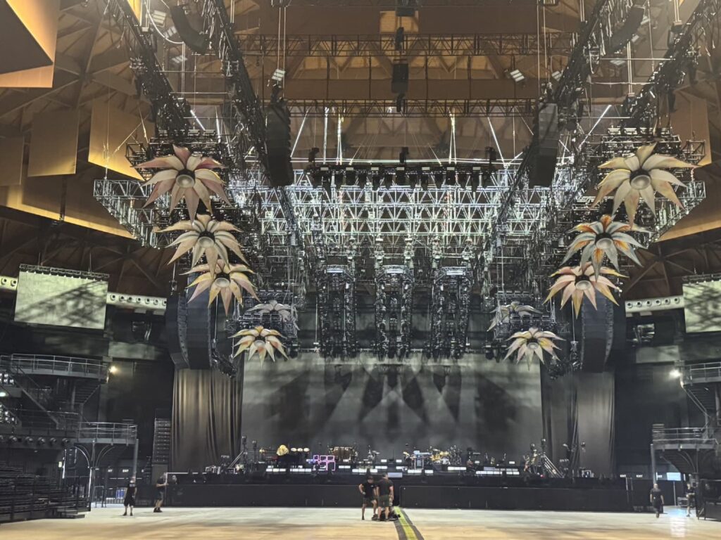Escenario de la gira PalaJova de Jovanotti con sistemas GSL de d&b audiotechnik y escenografía con flores móviles en un recinto cubierto.