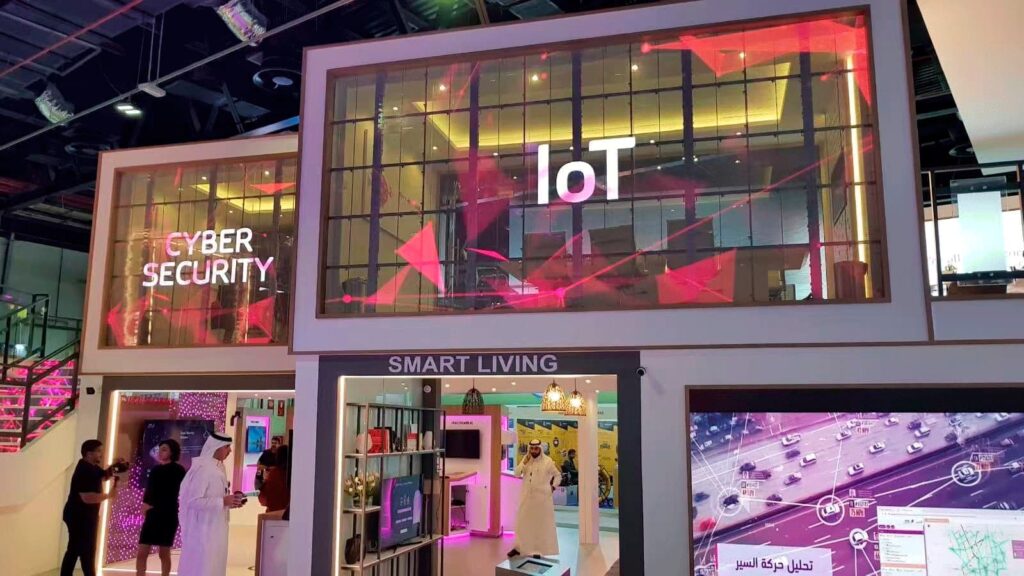 Pantallas LED transparentes de Traulux by Charmex en feria tecnológica, aplicadas en stands para mostrar contenido de IoT y ciberseguridad.