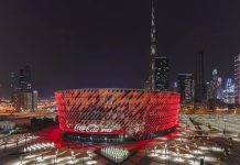 Vista nocturna del Coca-Cola Arena de Dubái iluminado en rojo, recinto multiusos equipado con sistemas de sonido d&b audiotechnik de la serie SL.