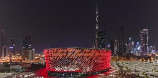 Vista nocturna del Coca-Cola Arena de Dubái iluminado en rojo, recinto multiusos equipado con sistemas de sonido d&b audiotechnik de la serie SL.