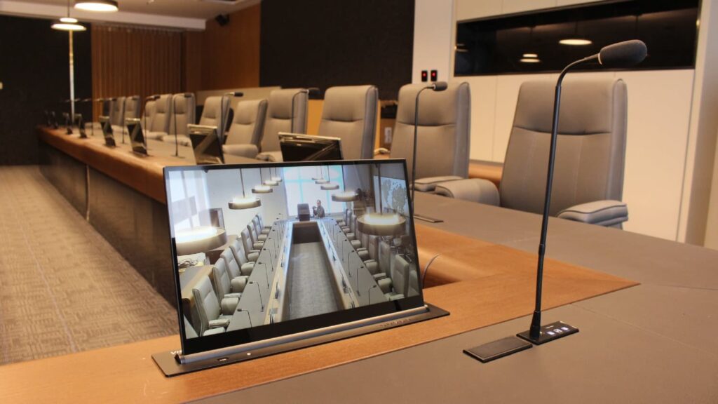 Primer plano de pantalla elevable HD ultrafina VISSONIC integrada en mesa de junta corporativa junto a micrófono empotrado para conferencias