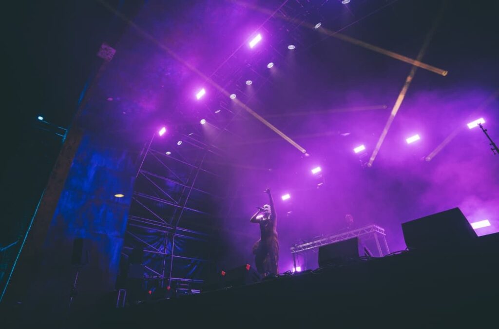 Escenario del Boomtown Festival 2025 con iluminación profesional en tonos violeta y haz de luces sobre el artista.