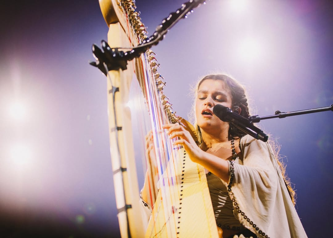 Amaia en el Cartuja Center CITE: interpretación con arpa y micrófono, primer plano bajo iluminación de concierto