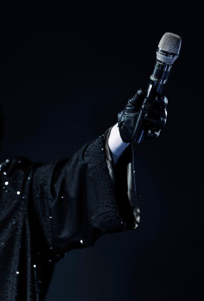 Sound Devices Astral en directo: primer plano de una mano con guante sosteniendo un micrófono inalámbrico sobre fondo oscuro.