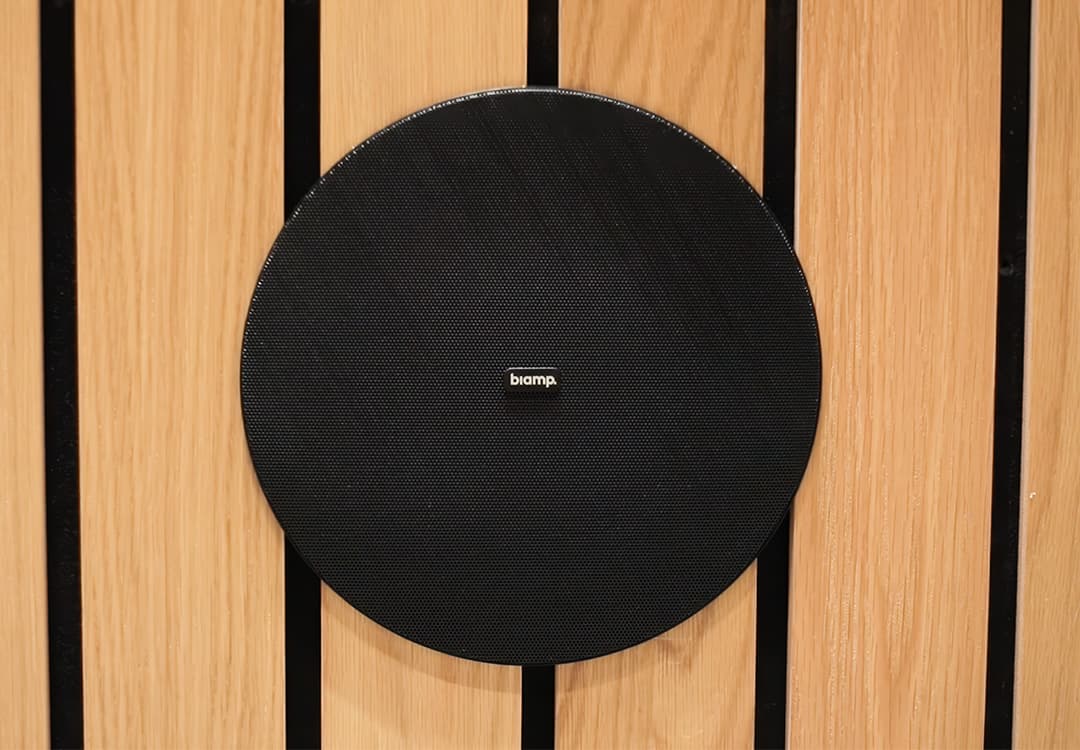 Altavoz Biamp instalado sobre panel de madera en una sala universitaria
