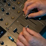 DJ ajustando los faders de un mezclador profesional durante una mezcla con múltiples decks.