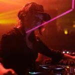 DJ pinchando toda la noche en cabina de club con luces magenta