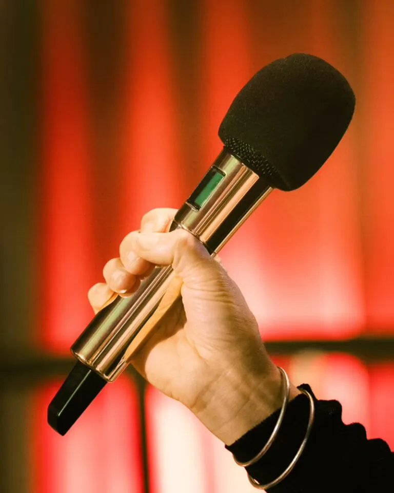 Sennheiser EW-DX gestiona 30 canales inalámbricos en Mic Drop Karaoke 3 Micrófono inalámbrico Sennheiser chapado en oro sostenido por un asistente en Mic Drop Karaoke