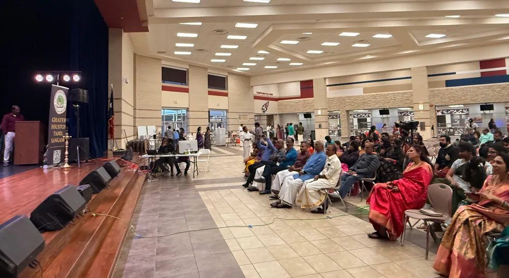 Público sentado ante el escenario del concurso Thirukkural con el cartel de Greater Houston Tamil Sangam.