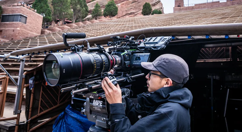 Operador ajusta una cámara cinematográfica con óptica de distancia focal variable frente al graderío de Red Rocks