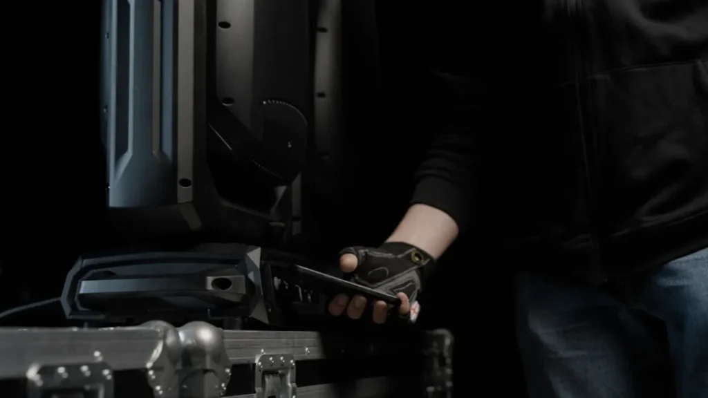 Cameo CONNECT digitaliza por NFC la configuración, el mantenimiento y el firmware de las luminarias 1 Técnico acercando un teléfono móvil a la base de una cabeza móvil Cameo apoyada sobre un flight case para transferirle la configuración por NFC