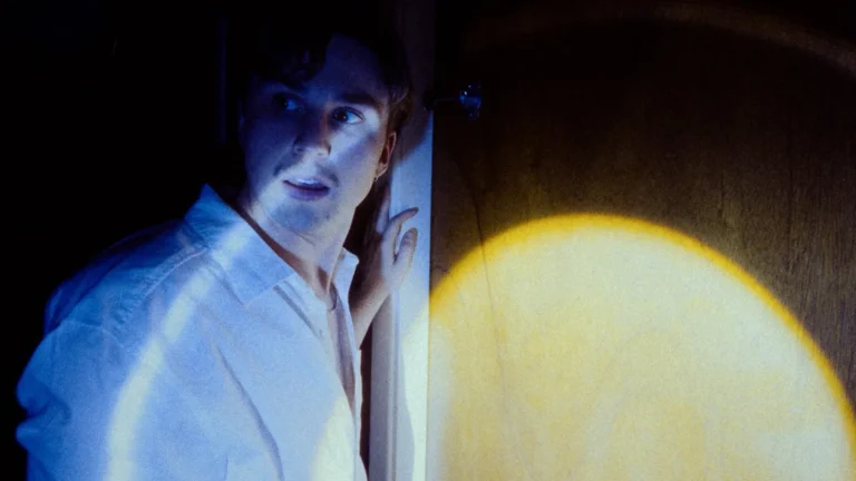 Actor apoyado en una pared de madera iluminada por una luz práctica en una escena de «Fire Alive»