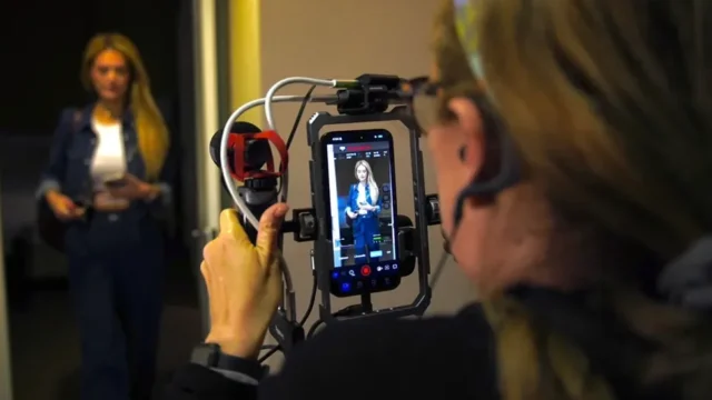 Operadora de cámara sostiene un iPhone montado en un armazón mientras graba a una integrante del reparto de «Legal Queens»; en la pantalla se ve la interfaz de Blackmagic Camera