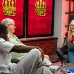 Tres colaboradores de The United Stand conversan en el set del canal, con pantallas rojas con el logotipo del programa al fondo.