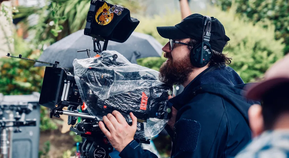 Deadheading, la comedia negra en gran formato premiada en los Sony Future Filmmaker Awards 2 Un operador sujeta una cámara de cine digital protegida con una funda de lluvia durante un rodaje exterior del cortometraje Deadheading