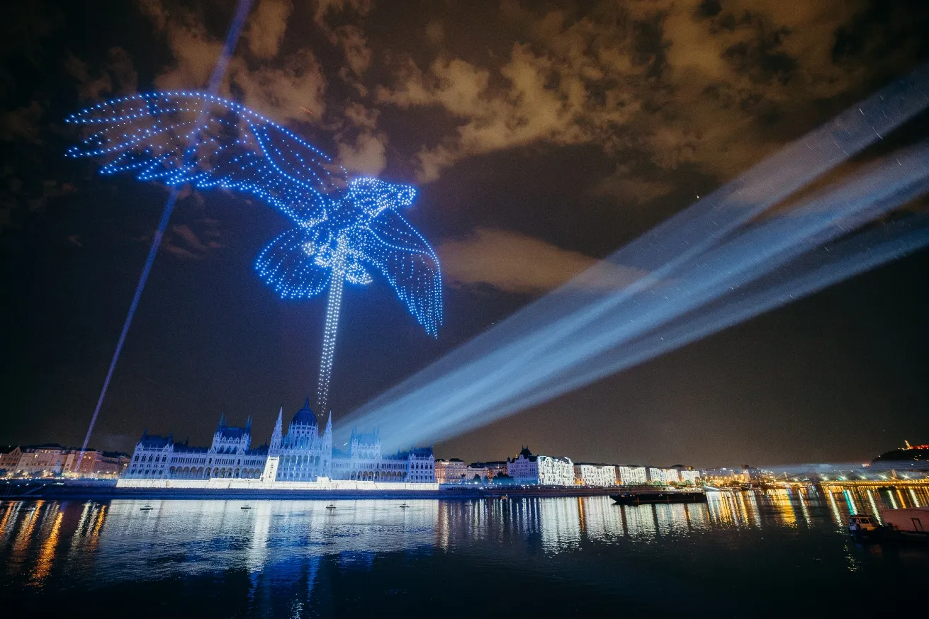 Figura de un ave formada por drones luminosos sobre el Parlamento de Hungría, con haces de luz cruzando el cielo nocturno de Budapest