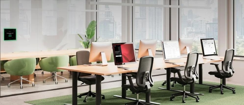 Gestión de espacios de trabajo: cómo optimizar la oficina híbrida con Biamp Evoko 2 Panel de reserva de sala con indicador verde de disponibilidad junto a puestos de trabajo con monitores en una oficina moderna