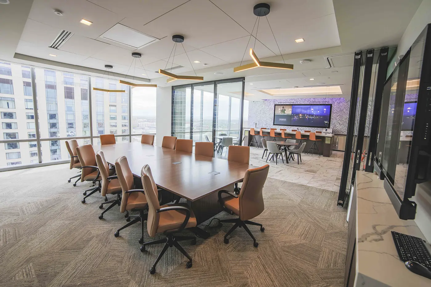Cómo Firmspace mejora la privacidad acústica en oficinas con Biamp 2 Sala de juntas vacía de una sede de Firmspace con mamparas de vidrio, moqueta, techo técnico y ventanales, junto a una zona común con pantalla