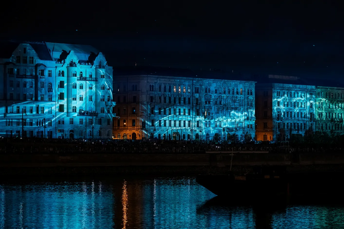 Videomapping en tonos azules sobre las fachadas de los edificios de la ribera de Pest, con el reflejo de la proyección en el agua del Danubio