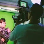 Un operador graba a un intérprete con chaqueta de lentejuelas frente a un croma verde iluminado durante el rodaje de «Vultures»