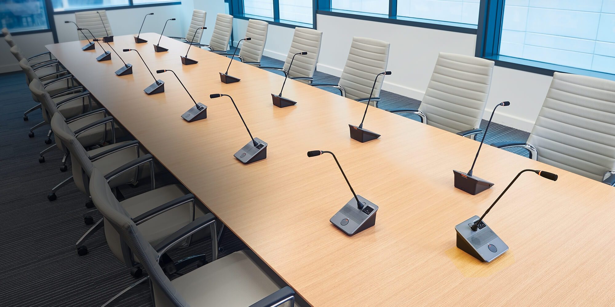 Audio en red para instalaciones profesionales: cómo diseñar sistemas Dante/IP escalables y fáciles de gestionar 5 Sala de reuniones corporativa equipada con micrófonos de sobremesa para conferencias y sistemas de audio profesional.