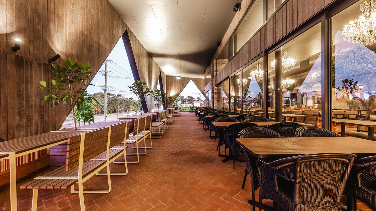 Terraza cubierta del Dakabin Hotel con bancos y mesas junto a la fachada acristalada del restaurante