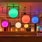 Luminarias esféricas de gran formato en verde, naranja, azul y magenta, enmarcadas en estructuras cúbicas de madera en el techo de Ametller Origen Via Laietana
