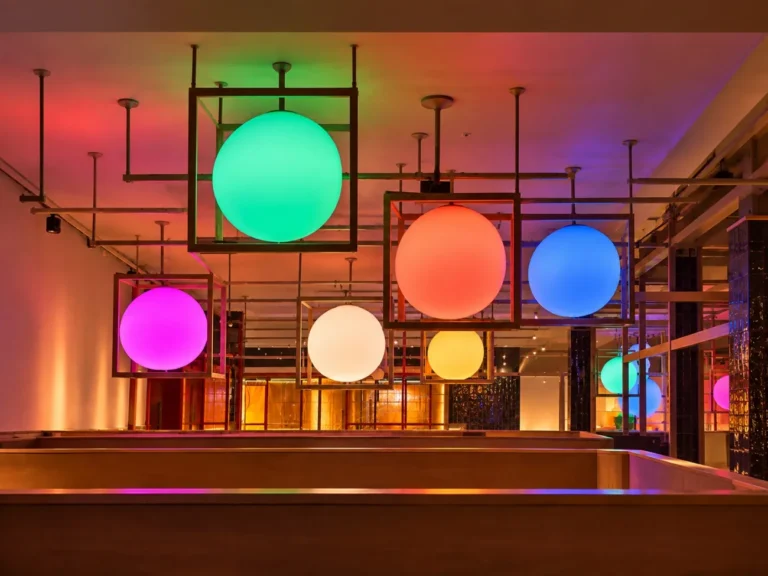 Luminarias esféricas de gran formato en verde, naranja, azul y magenta, enmarcadas en estructuras cúbicas de madera en el techo de Ametller Origen Via Laietana