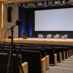 Micrófono de medición acústica sobre trípode en un auditorio durante la evaluación de la inteligibilidad de la palabra