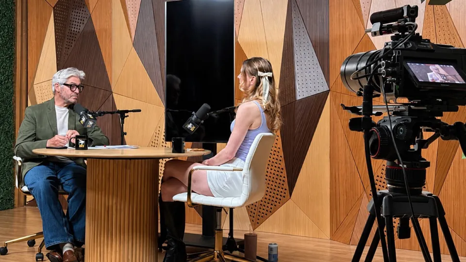 Buzz Leer entrevista a una invitada en un plató de Glendale Podcast Studio, con una cámara sobre trípode en primer plano